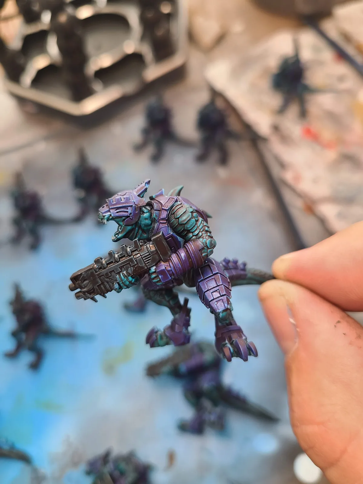A colorful painted creature miniature held above the workbench