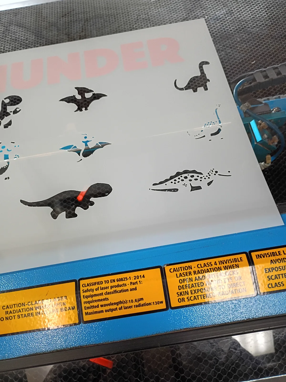 Dinosaur-shaped cutouts on a sheet inside a laser cutter