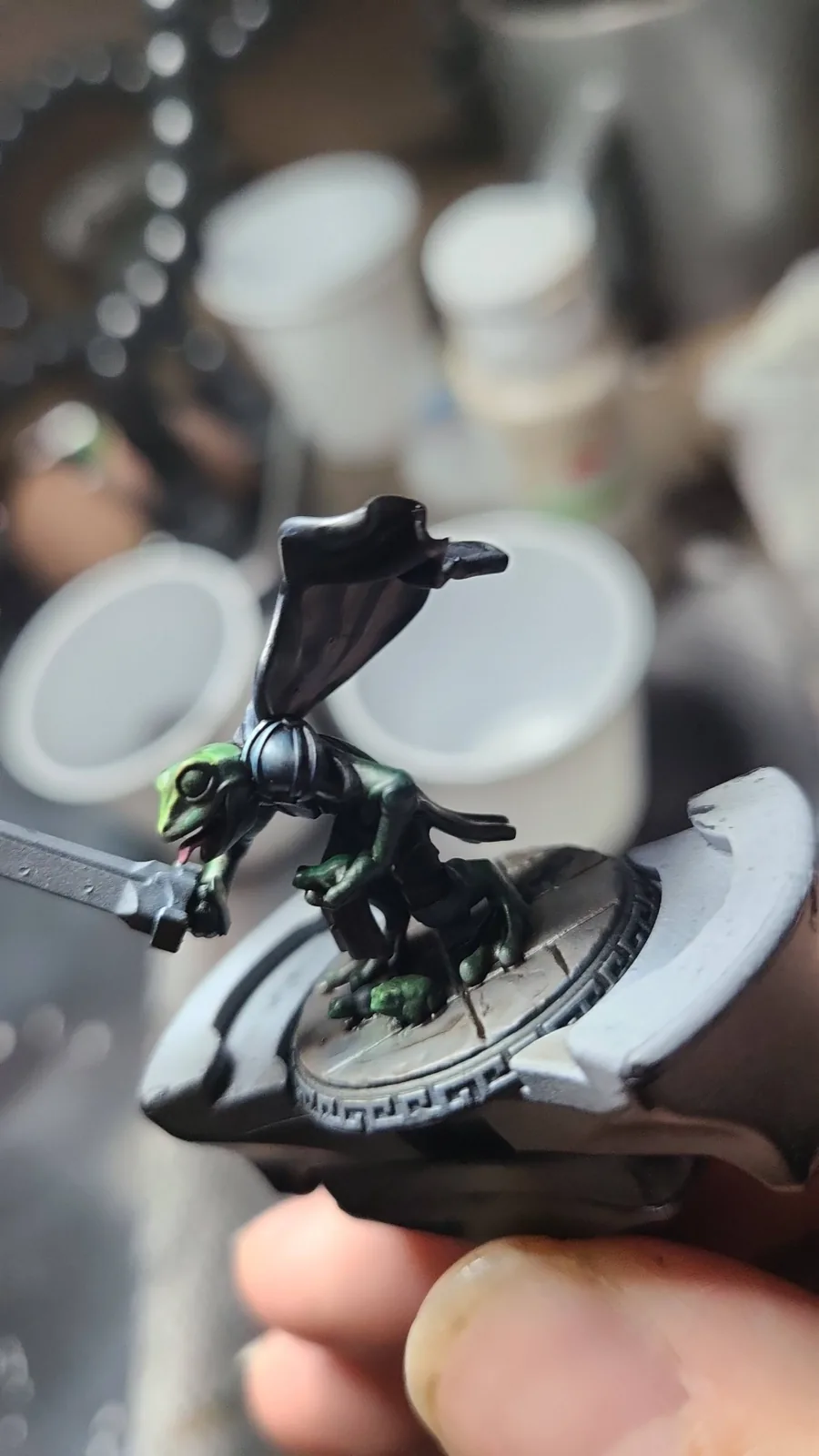 A painted fantasy miniature held in front of painting supplies